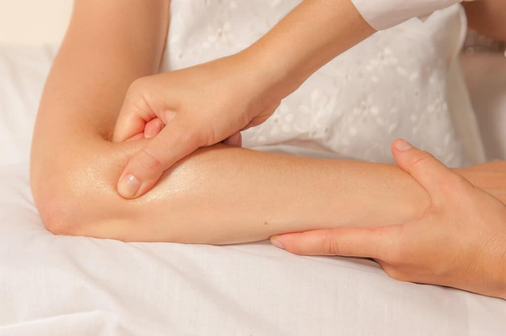 Bodyworker applies pressure with thumb and hand on client's  trigger points in forearm, providing relief for tennis elbow.
