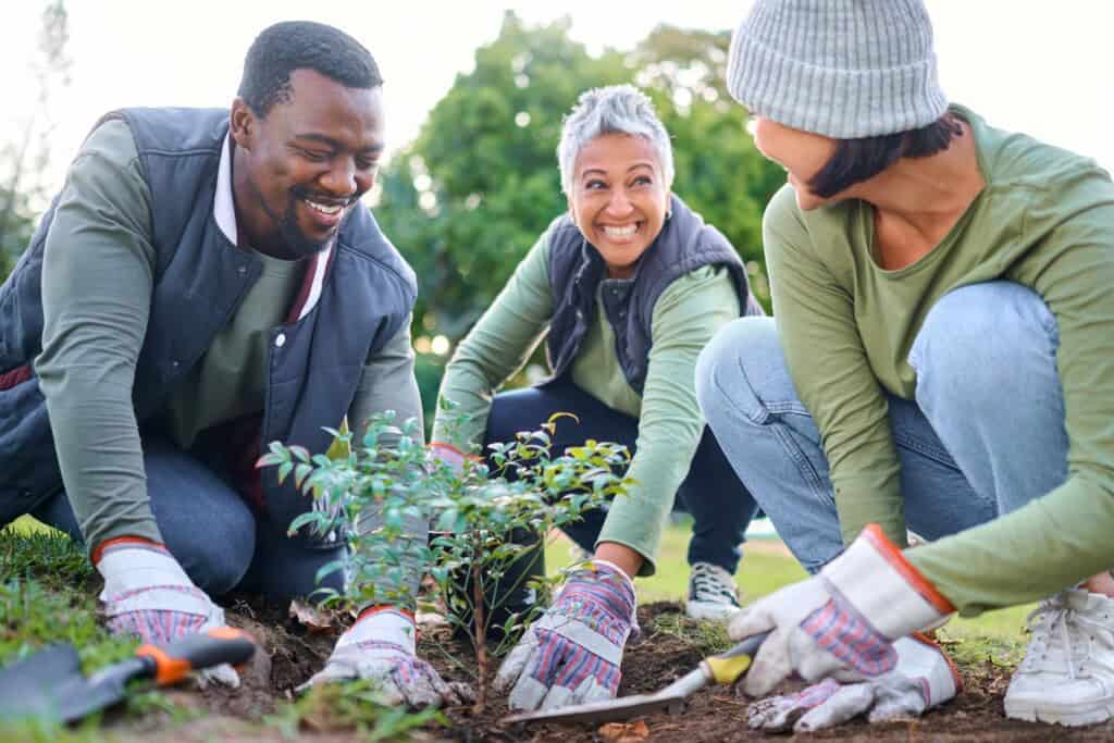 Two women and one man happily gardening together in a park.