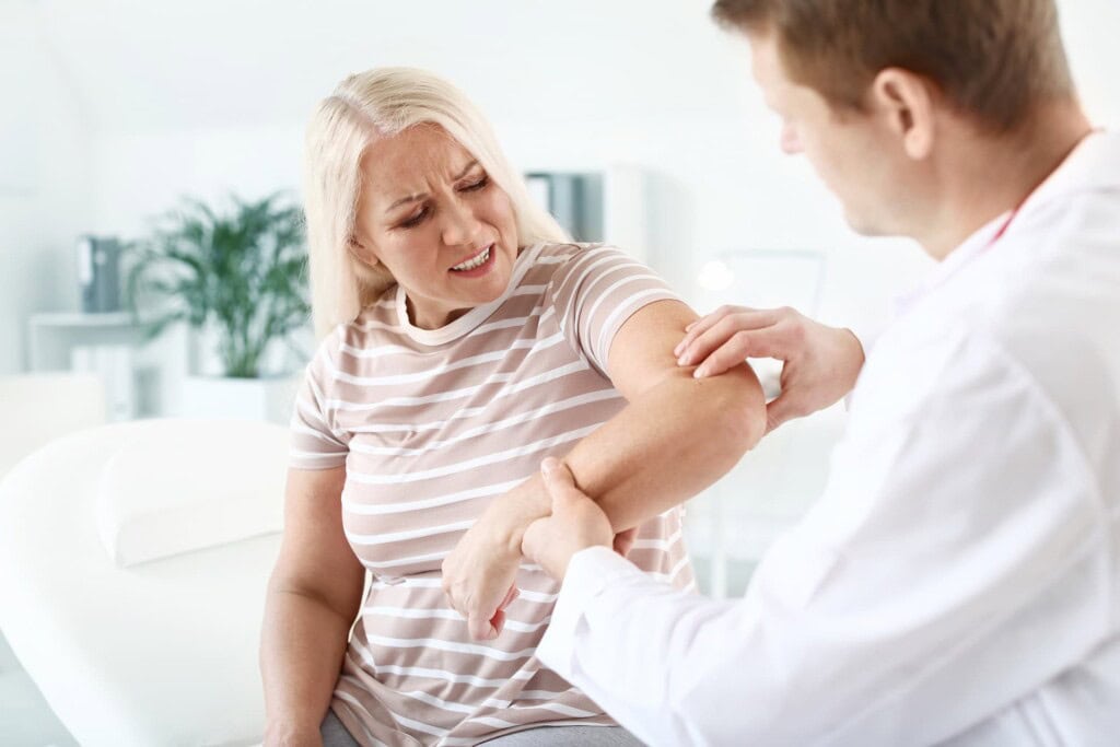 Therapist examining a mature woman's elbow who is suffering with elbow joint pain. 