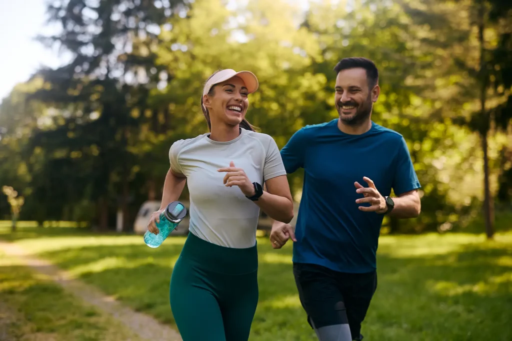 Smiling man and woman jogging together on a scenic trail, enjoying an active and healthy lifestyle.
