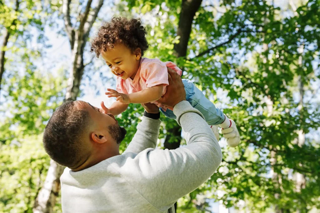 Father lifting his young child in the air while smiling, enjoying pain-free shoulder movement outdoors.