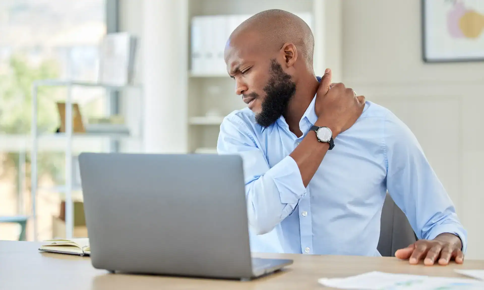 Man sitting at his computer holding his neck and shoulder due to stress-related muscle tension.