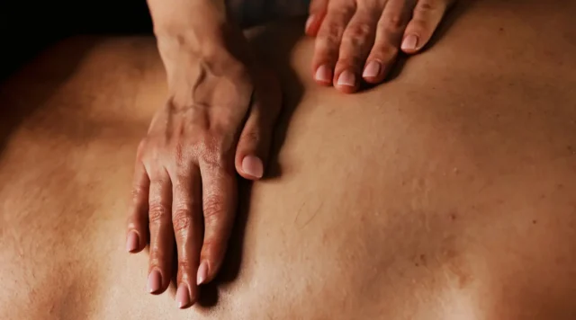 Close-up of a therapist's hands applying focused pressure to a client's back during fascia-focused bodywork.