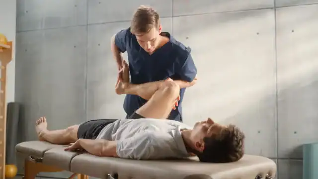 Physical therapist gently bending a patient's knee during a rehabilitation session on a treatment table.